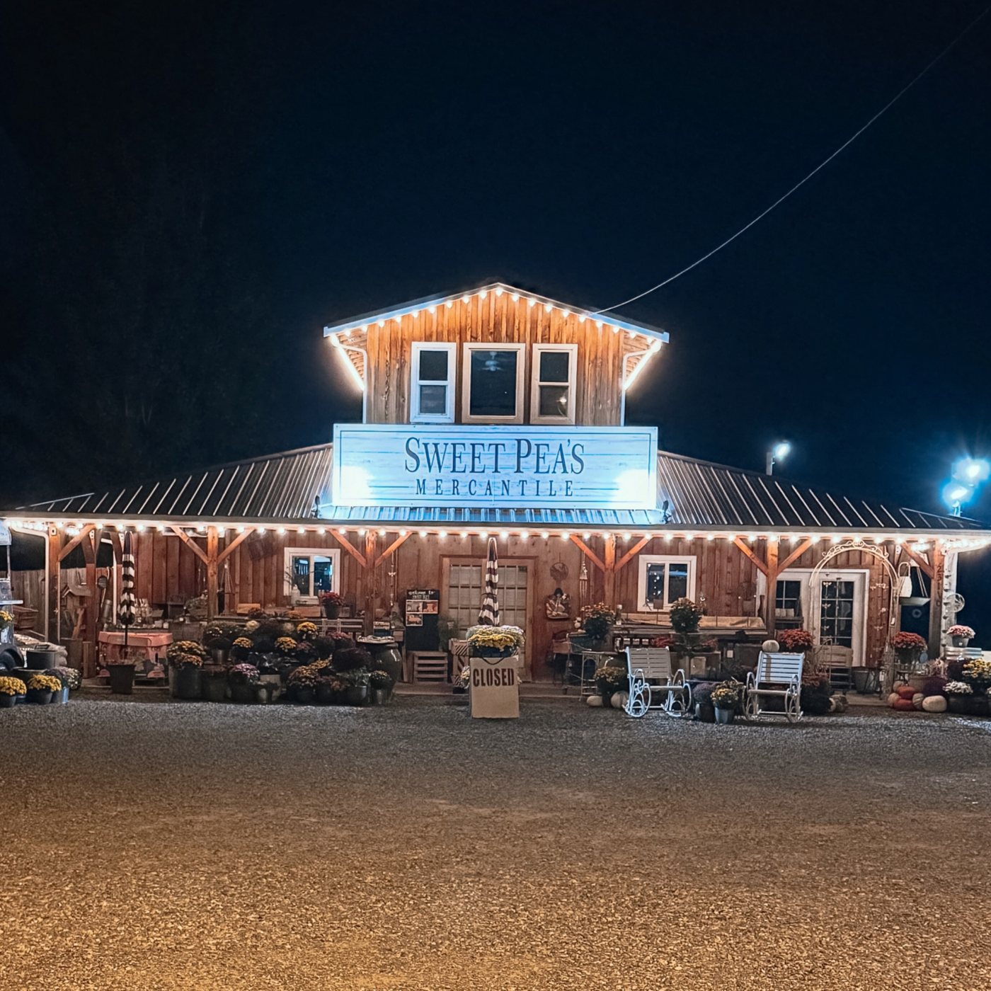 Sweet Pea’s Mercantile’s rustic wooden storefront glowing with twinkling lights on an autumn evening